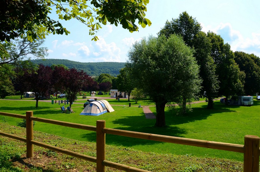 grand espace vert avec arbres, toiles de tentes et une barrière bois en premier plan